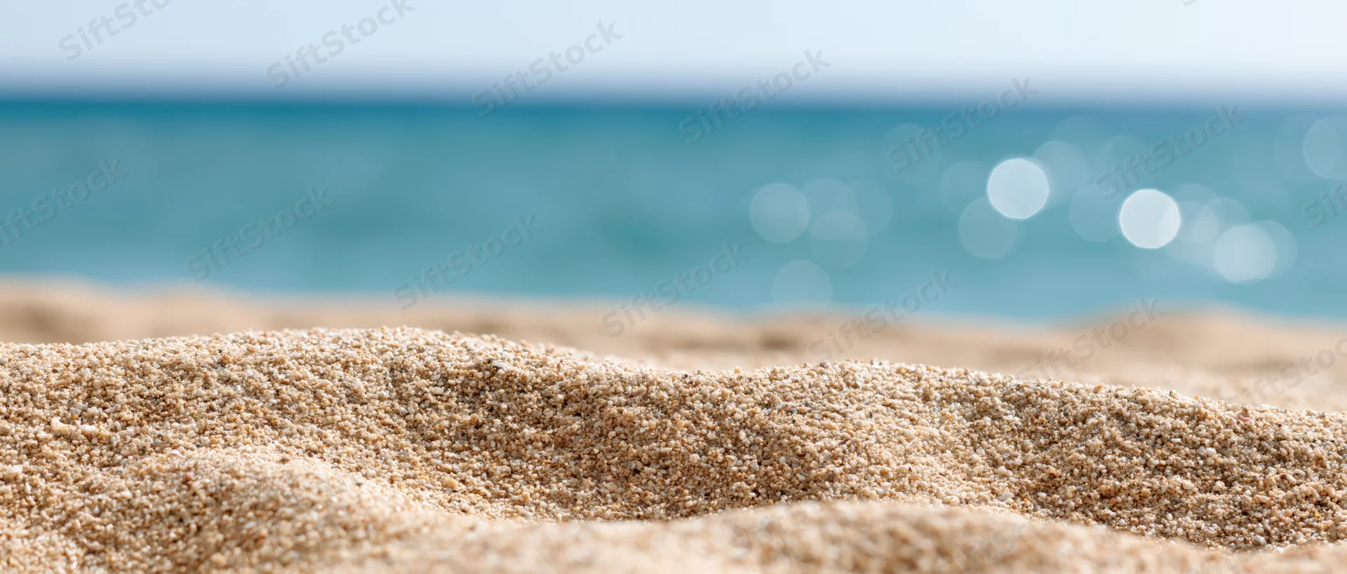Close-up of sun-warmed beach sand in foreground with blurred ocean and sky in background