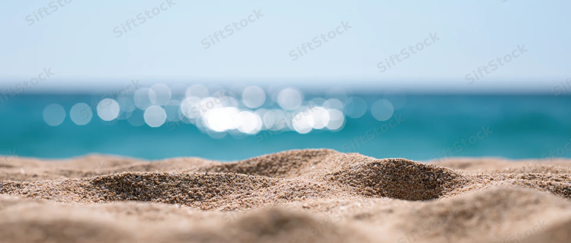 Close-up of textured beach sand in foreground with blurred ocean and sky in background