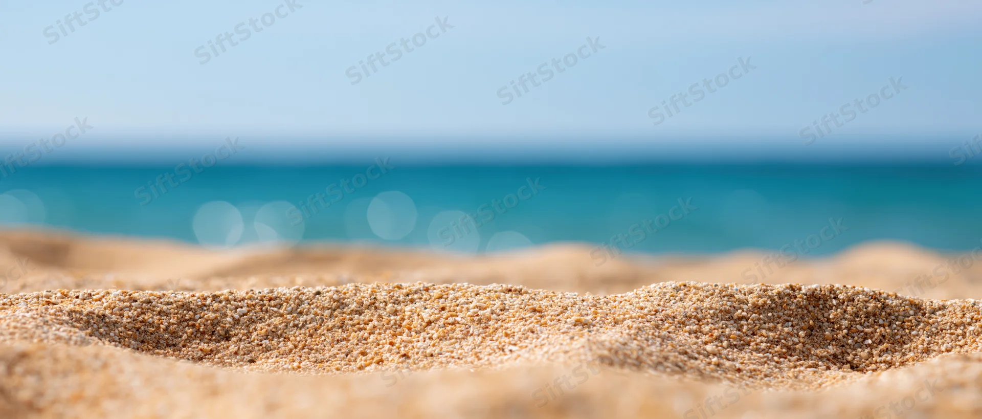 Closeup of textured beach sand in foreground with blurred ocean and sky beyond