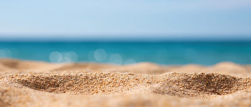 Closeup of textured beach sand in foreground with blurred ocean and sky beyond