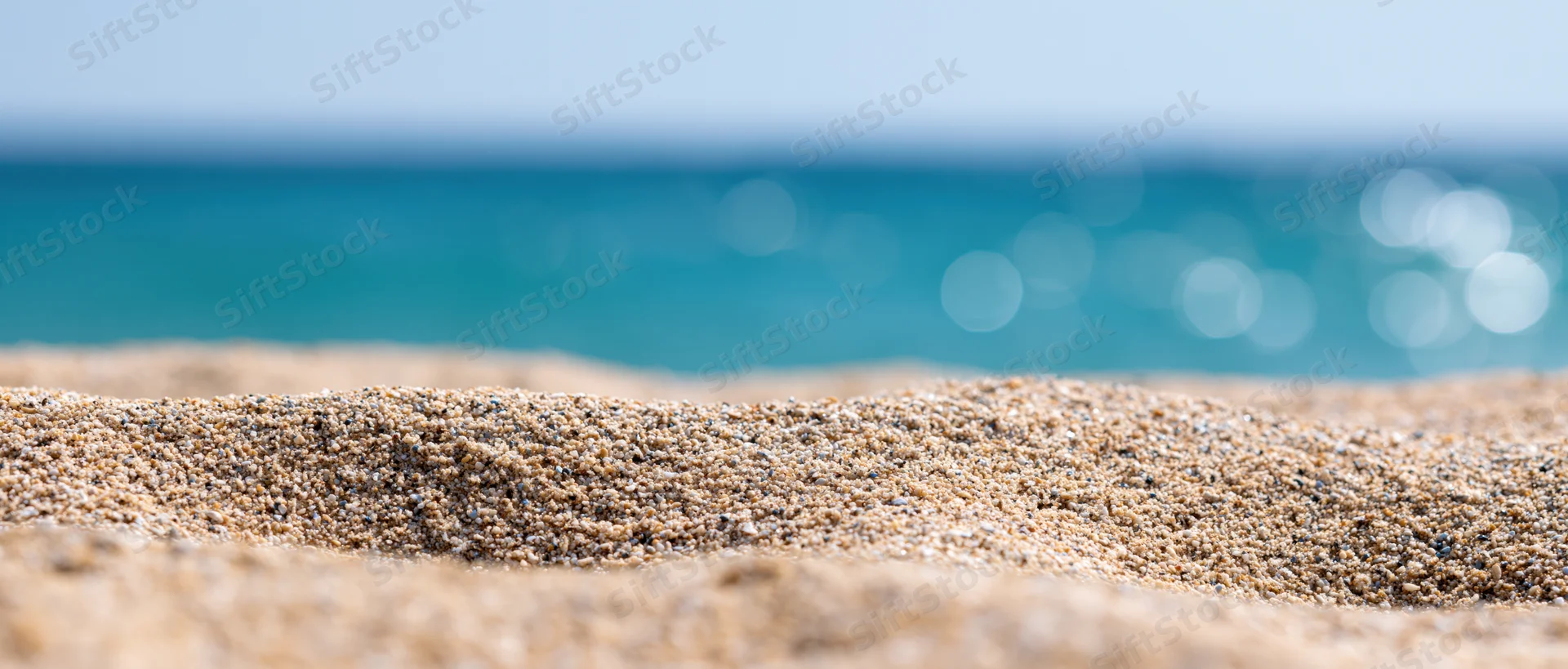 Close-up of textured beach sand in foreground with blurred ocean and sky beyond