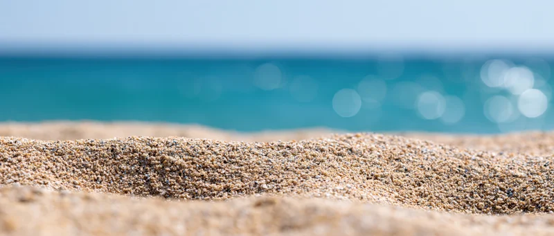 Close-up of textured beach sand in foreground with blurred ocean and sky beyond