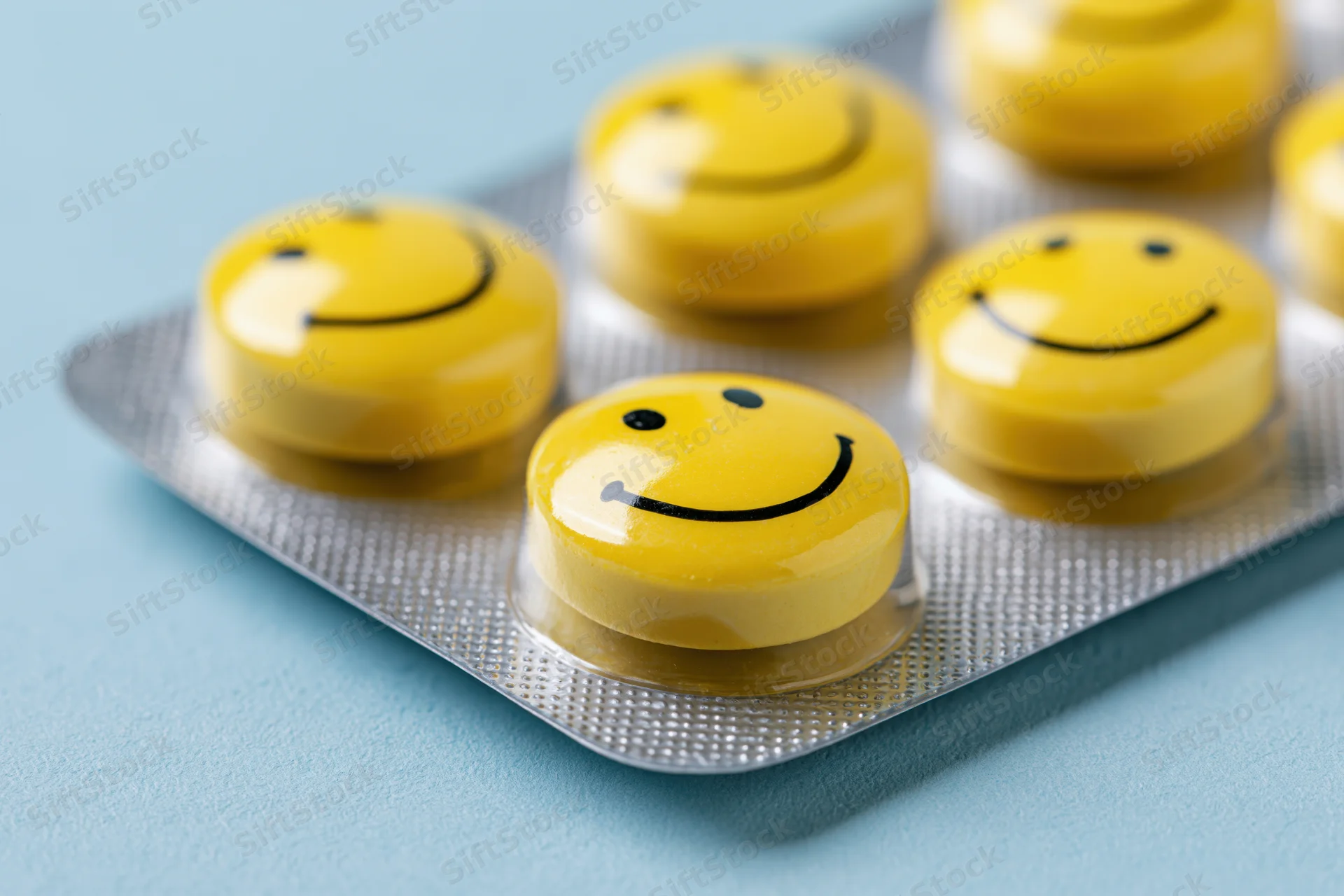 Yellow round pills with smiley faces in a blister pack on a blue surface