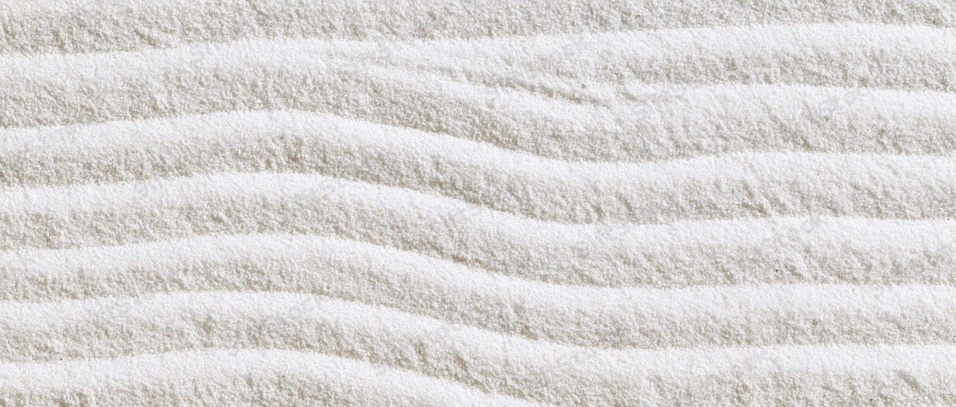 Raked white sand forming wavy lines in a Japanese garden setting