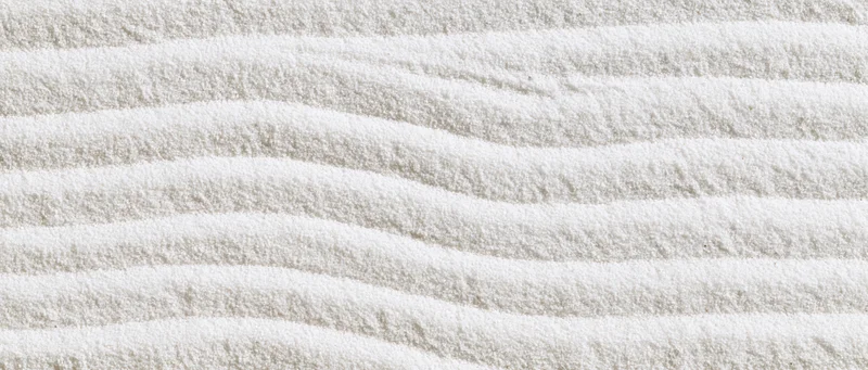 Raked white sand forming wavy lines in a Japanese garden setting