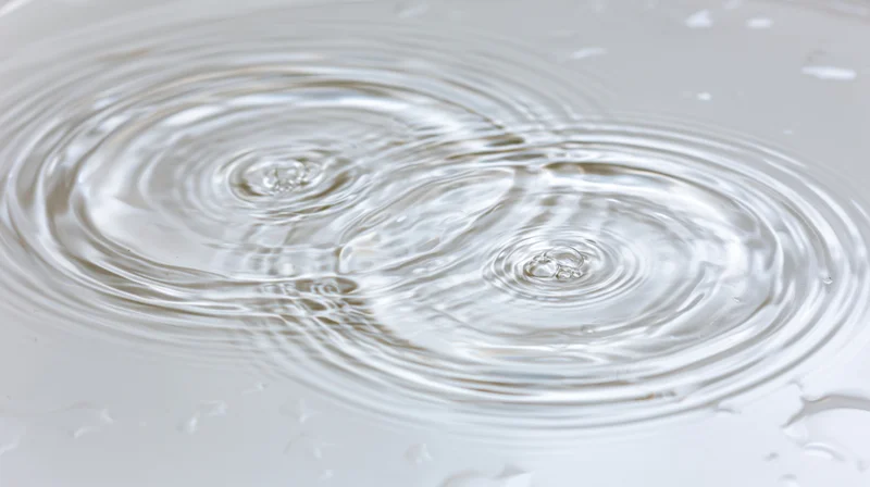 Close-up overhead view of ripples spreading on a shallow clear water surface