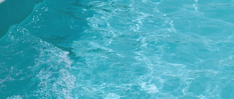 Overhead closeup of clear turquoise pool water surface with ripples and bubbles near the edge