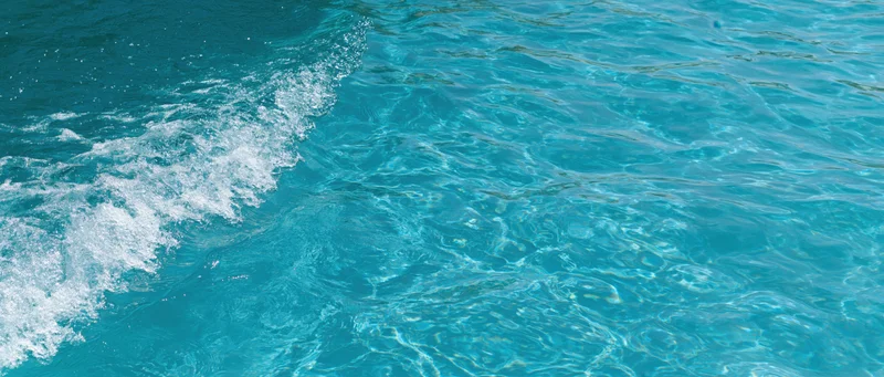 Overhead closeup of clear turquoise pool water surface with ripples and foam