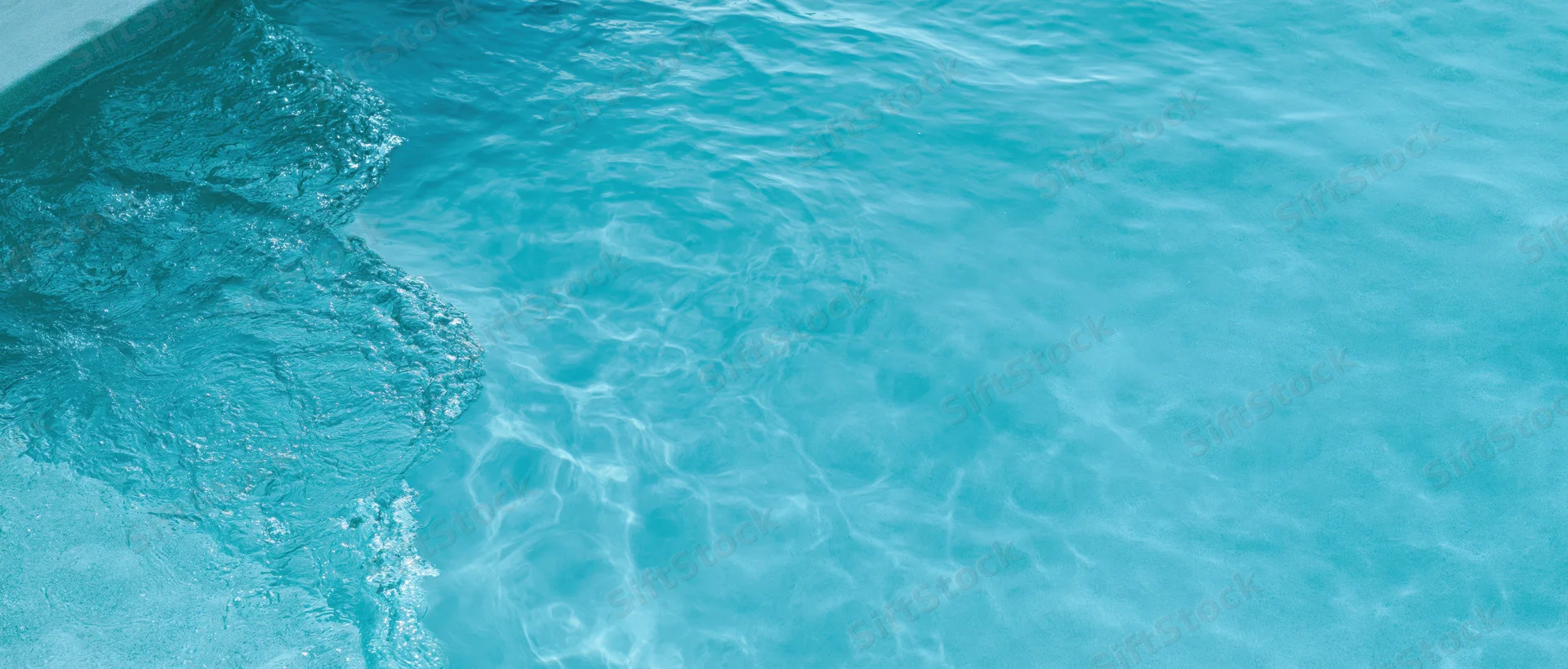 Overhead closeup of clear turquoise pool water surface with ripples and light reflections