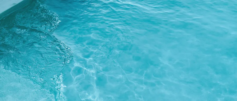 Overhead closeup of clear turquoise pool water surface with ripples and light reflections