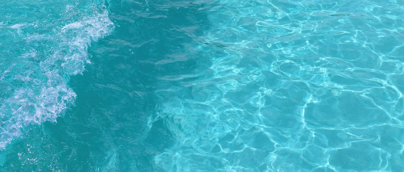Overhead closeup of clear turquoise pool water surface with ripples and light reflections