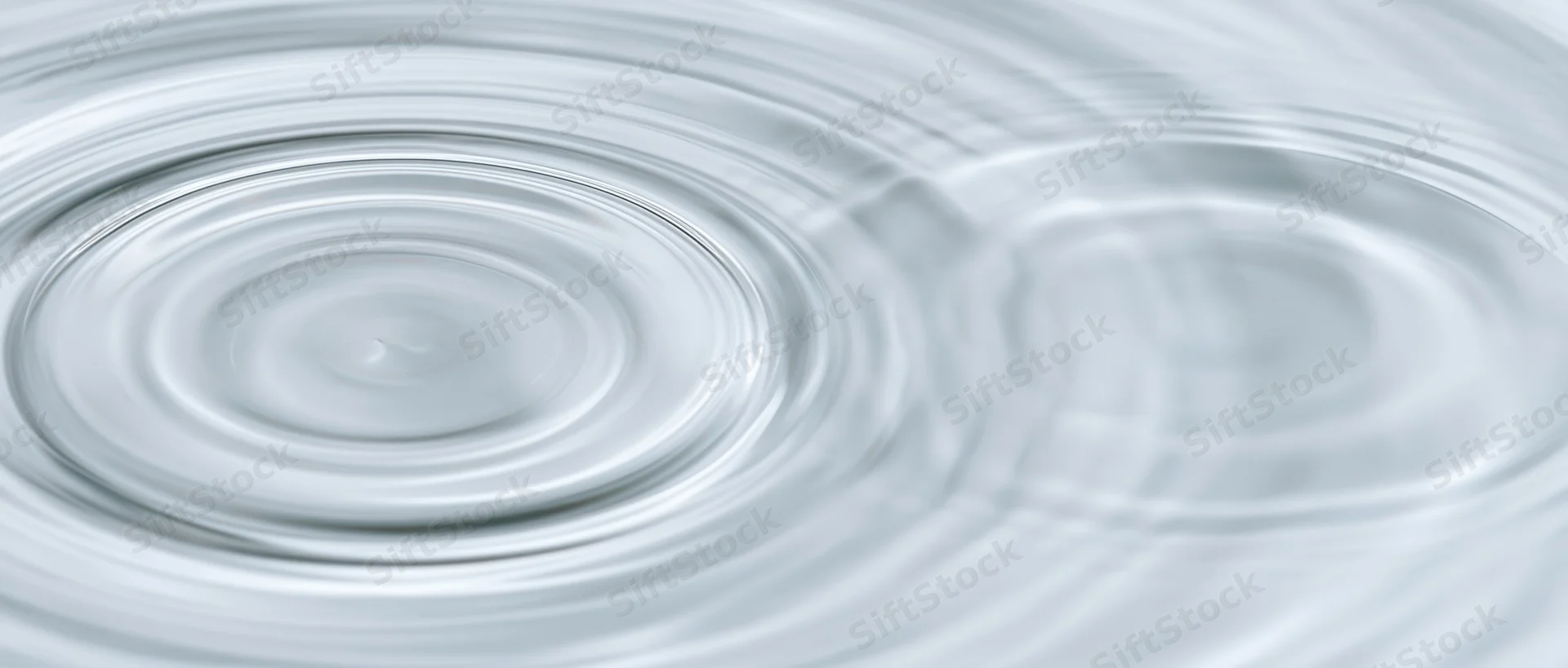 Concentric ripples spreading across a calm water surface from an overhead closeup view