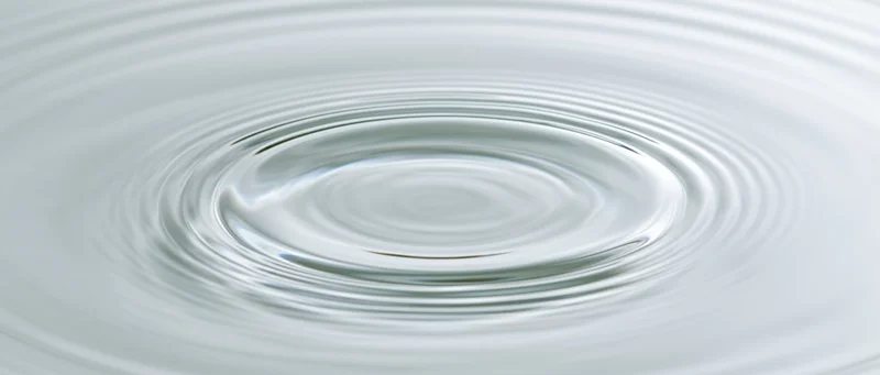 Concentric ripples spreading across a calm water surface from a central droplet impact