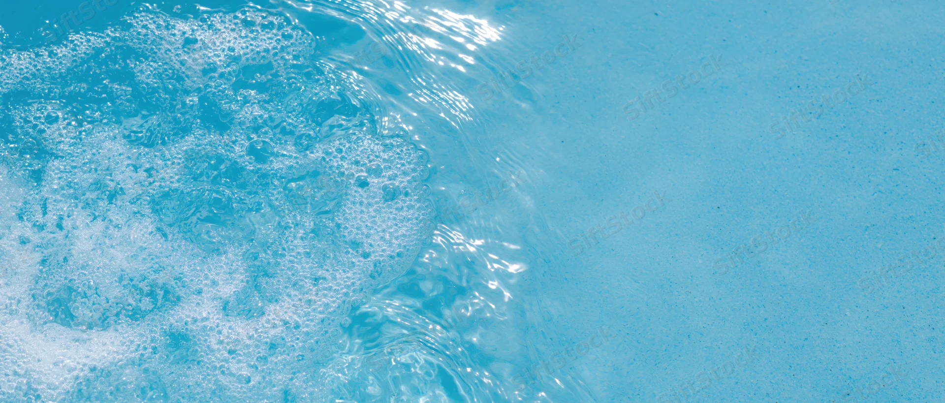 Overhead closeup of rippling clear water with foam and bubbles on a blue surface