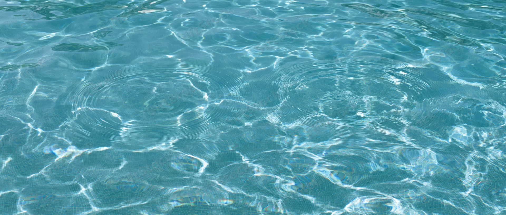Overhead closeup of gently rippling swimming pool water surface with light reflections