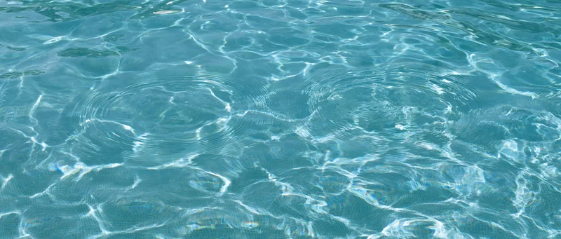 Overhead closeup of gently rippling swimming pool water surface with light reflections