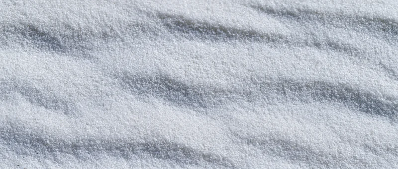 Close-up overhead view of smooth white beach sand with shallow ripples and soft shadows