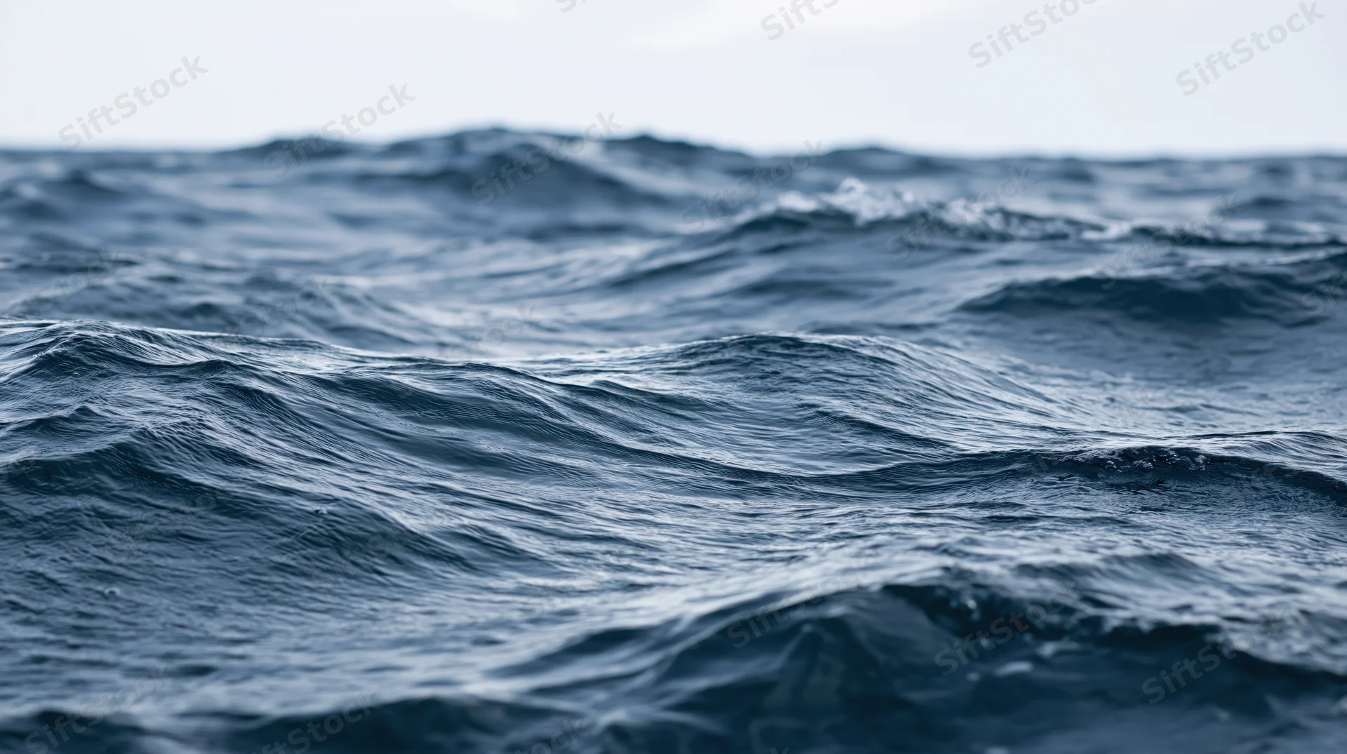 Close-up of deep ocean waves undulating at surface level under overcast sky