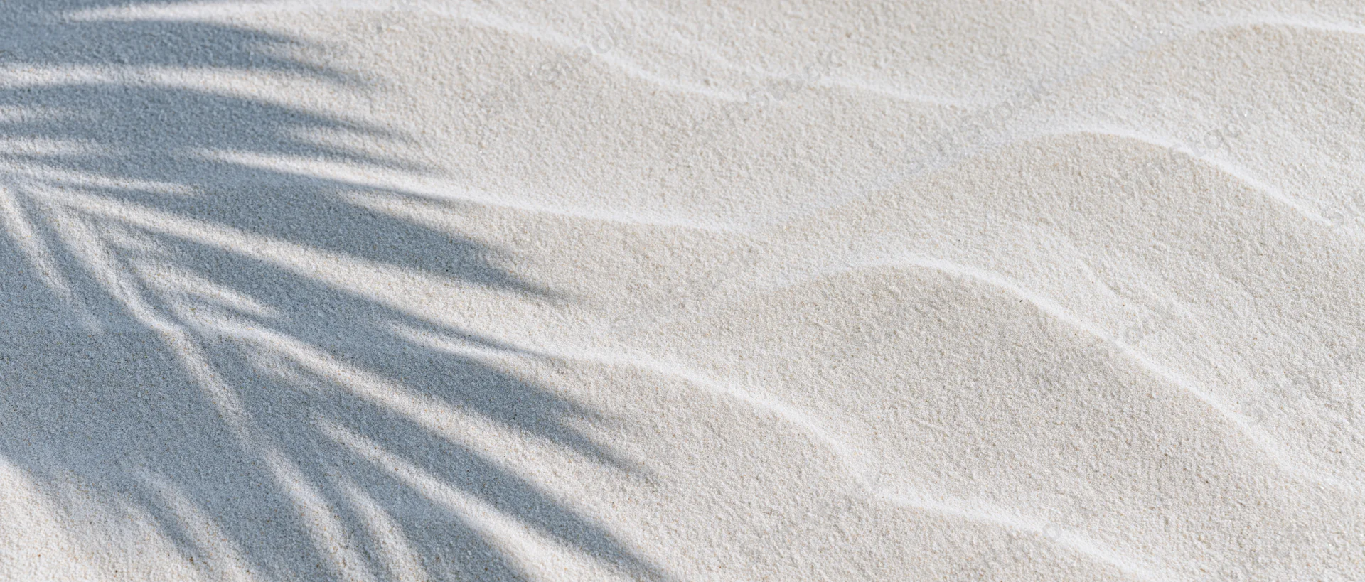 Close-up of white beach sand with palm leaf shadows and gentle ripples