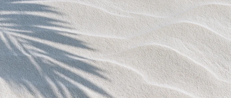 Close-up of white beach sand with palm leaf shadows and gentle ripples