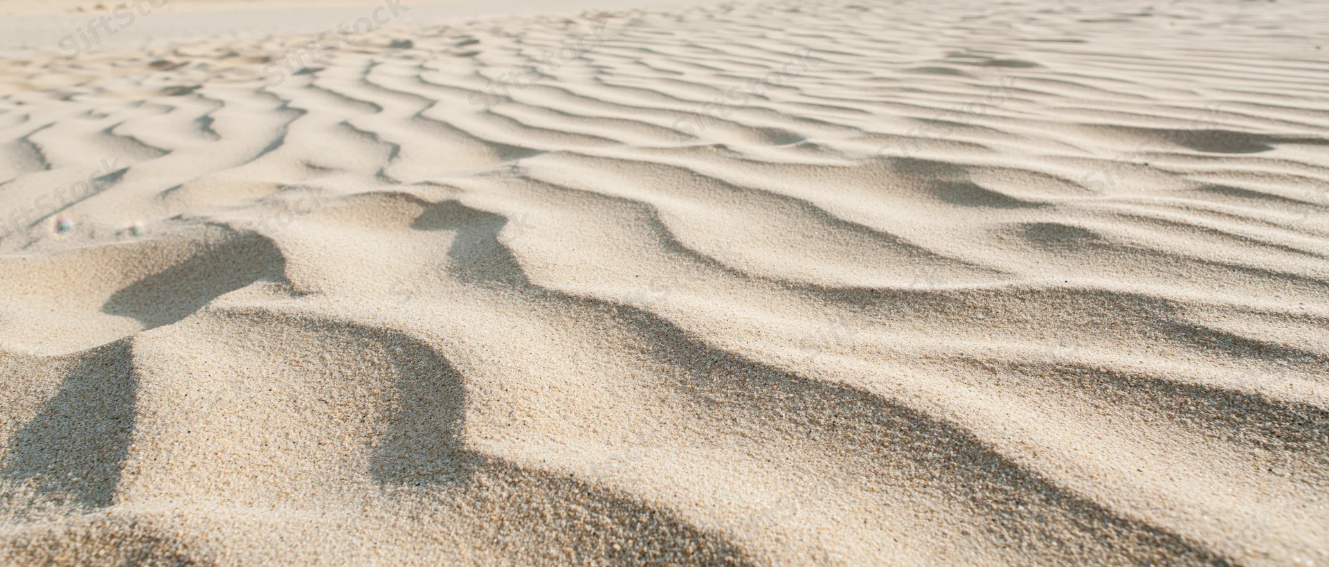 Close-up of rippled dry beach sand under sunlight