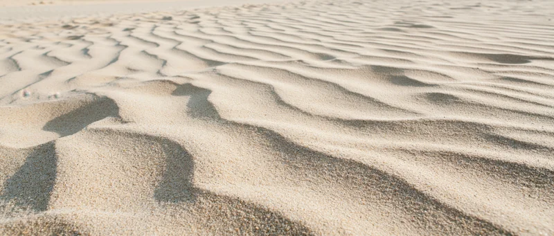 Close-up of rippled dry beach sand under sunlight