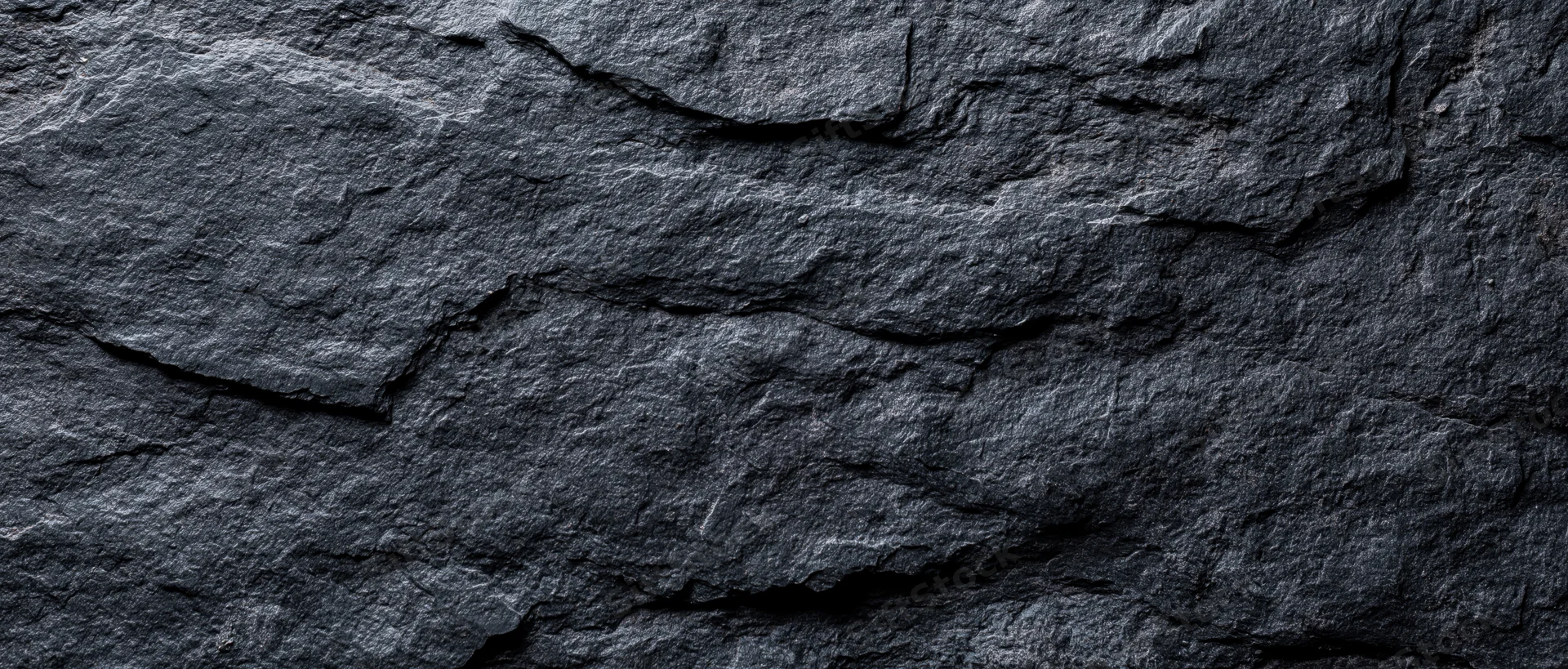 Close-up of dark slate stone wall surface with natural cracks and layers