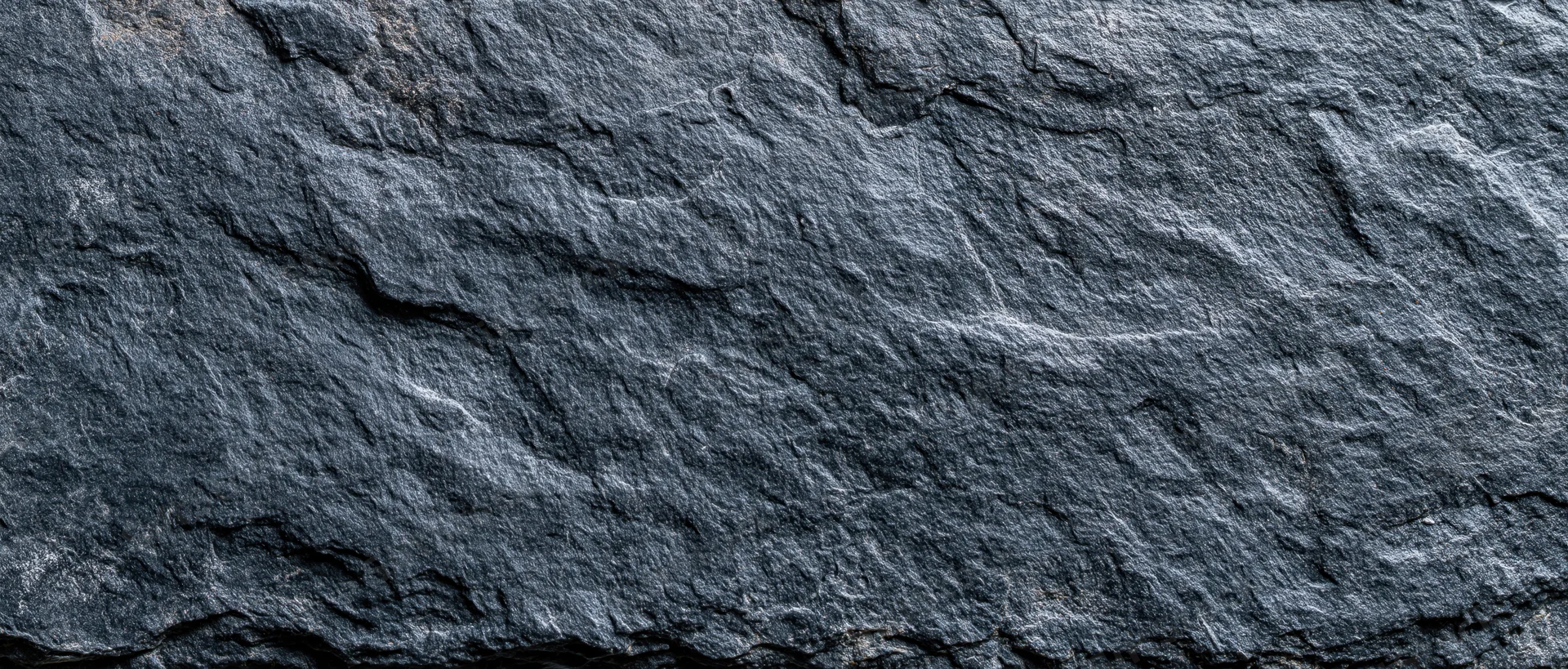Close-up of dark slate stone wall surface filling the frame with natural texture and cracks