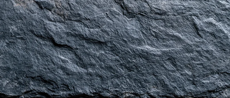 Close-up of dark slate stone wall surface filling the frame with natural texture and cracks
