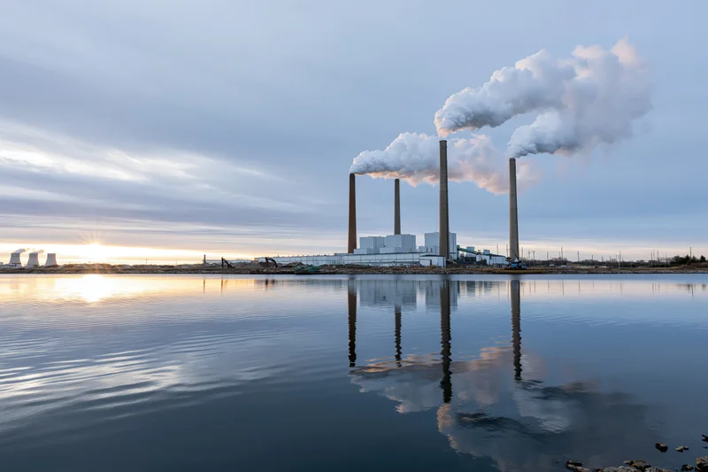 Coal-fired power plant with smokestacks emitting steam over a river at sunset