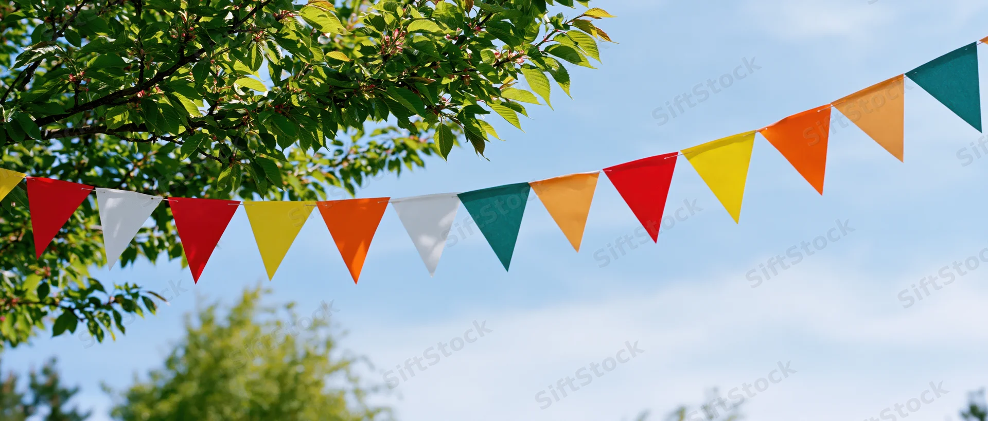 Colorful triangular paper bunting flags strung on a line across a garden under a tree on a sunny day