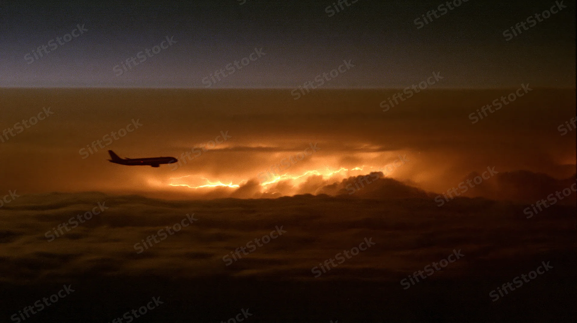 Commercial airplane flying above storm clouds at dusk with lightning flashing below