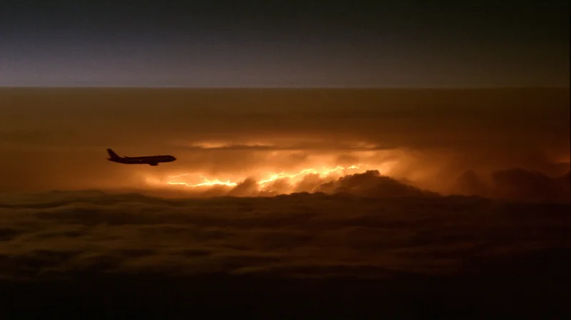 Commercial airplane flying above storm clouds at dusk with lightning flashing below