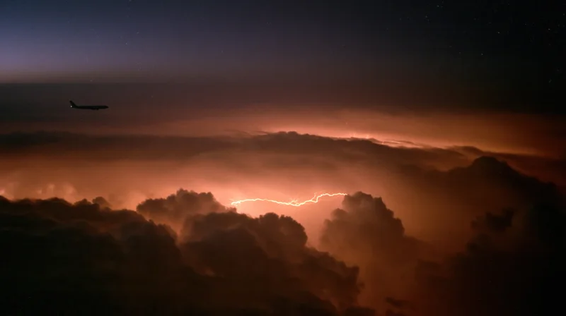 Commercial passenger jet flying above storm clouds at night with lightning below