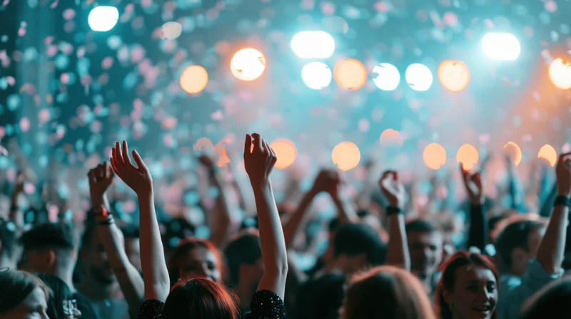 Crowd of people with arms raised at an indoor concert event under colorful stage lights