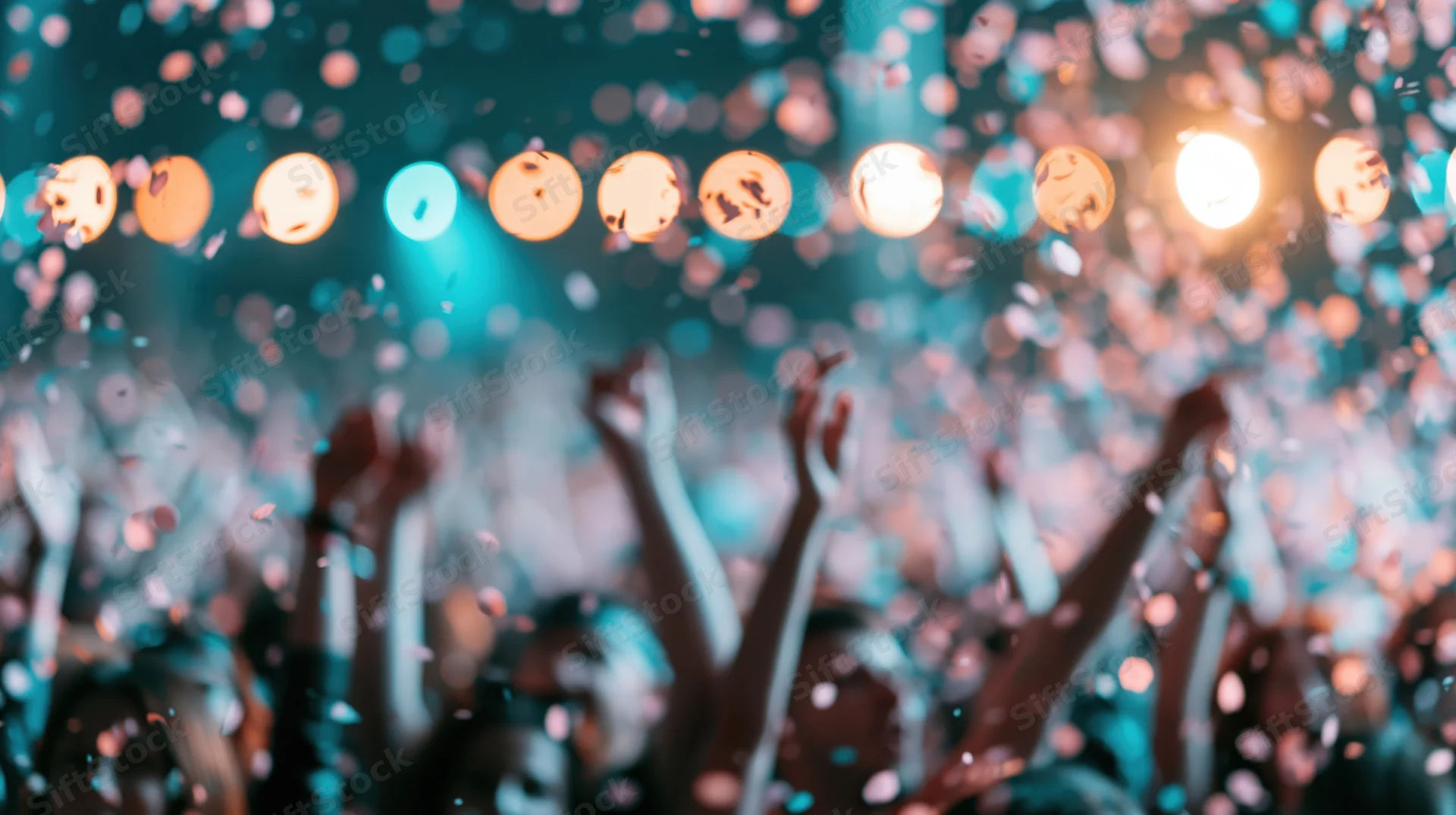Crowd celebrating with arms raised at indoor event under stage lights and falling confetti