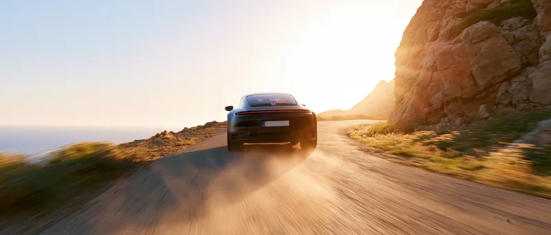 Black sports coupe driving away on winding coastal road at sunset