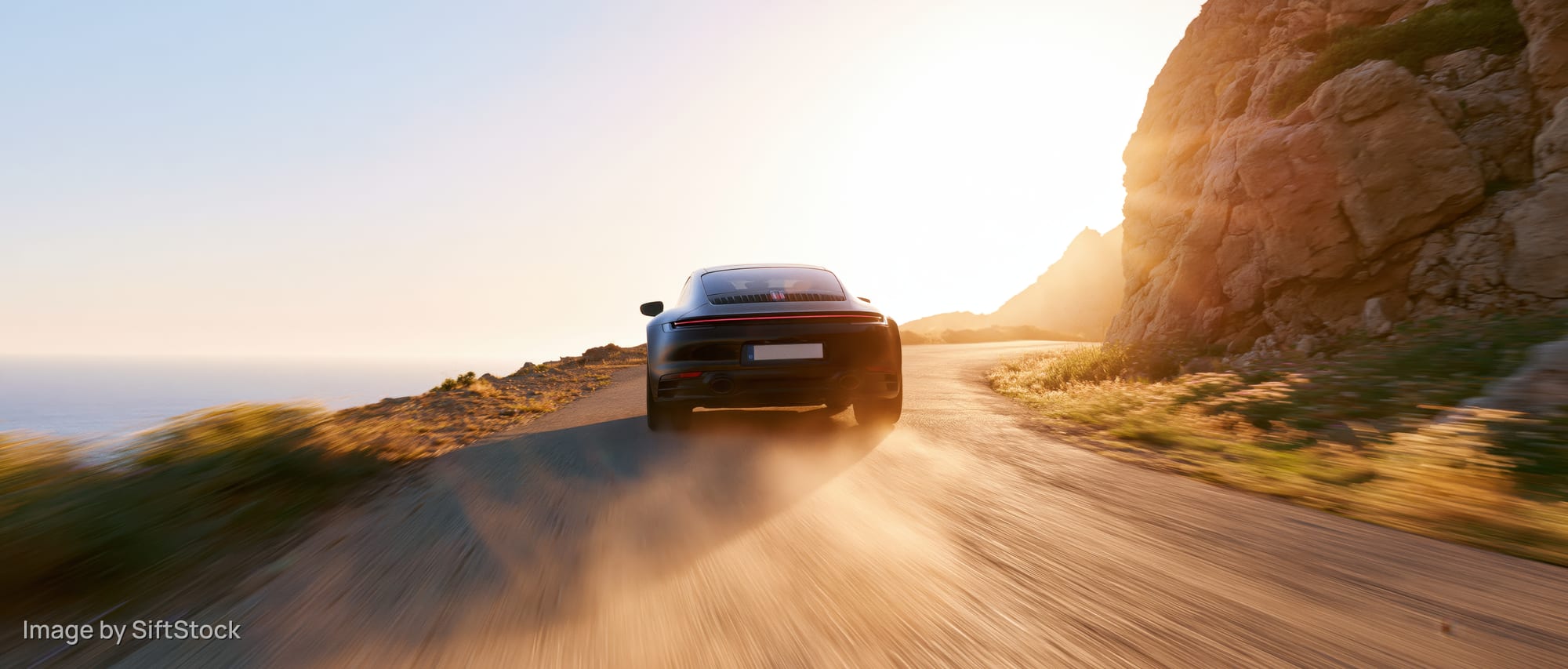 Black sports coupe driving away on winding coastal road at sunset