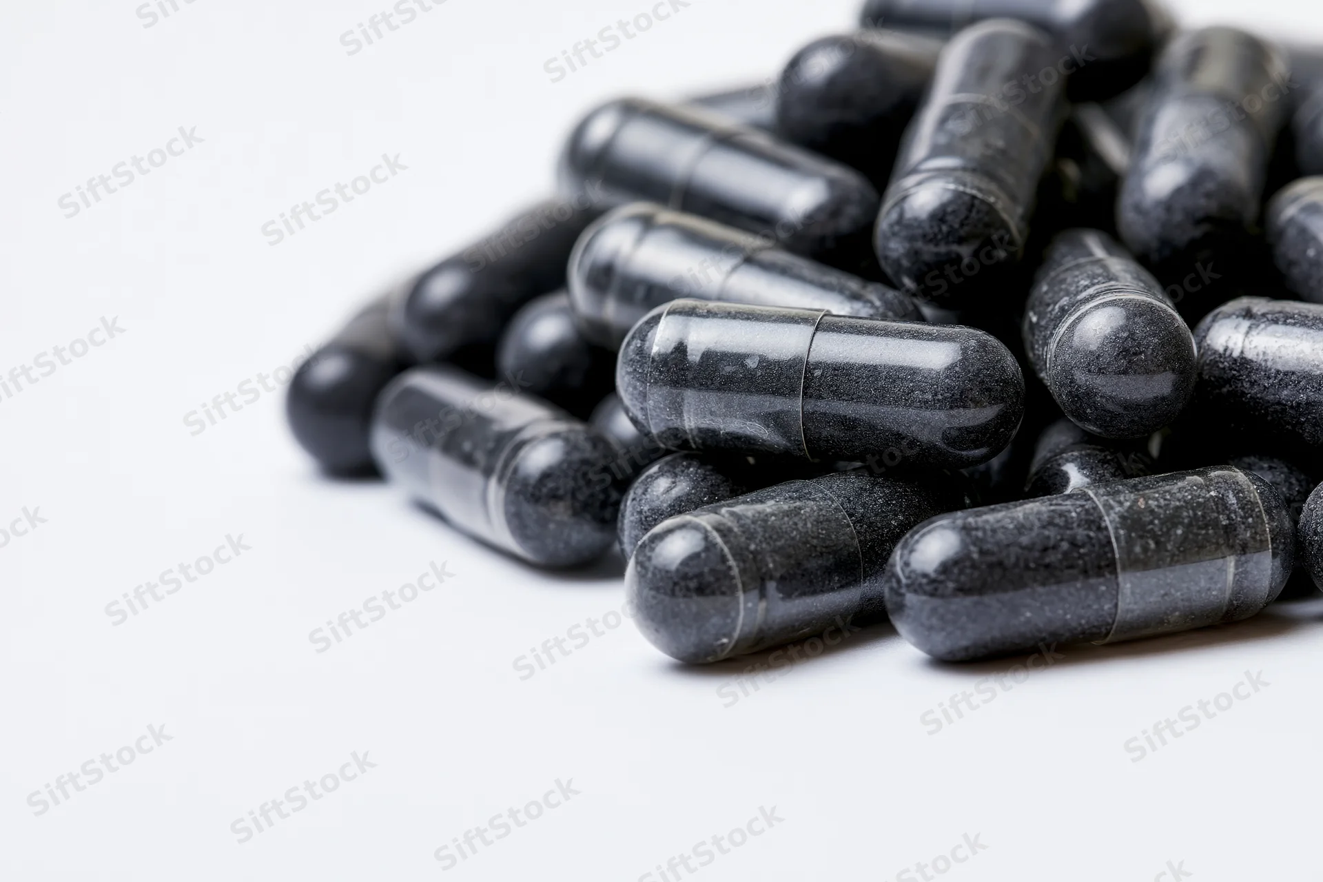 Pile of dark charcoal and grey supplement capsules on white background