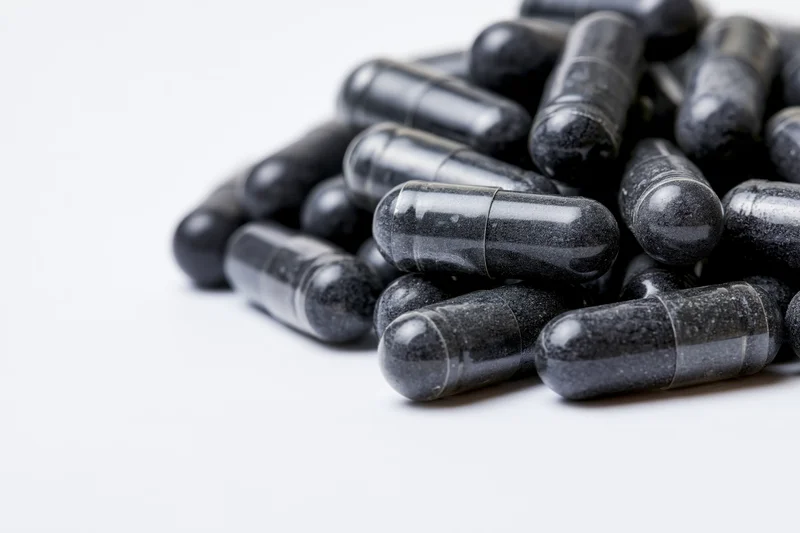 Pile of dark charcoal and grey supplement capsules on white background