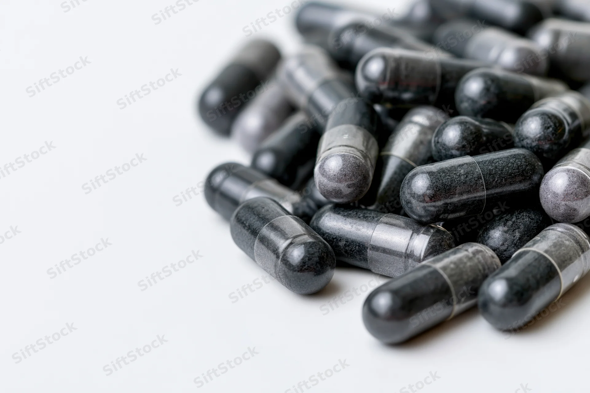 Dark charcoal and grey supplement capsules scattered loosely on white surface
