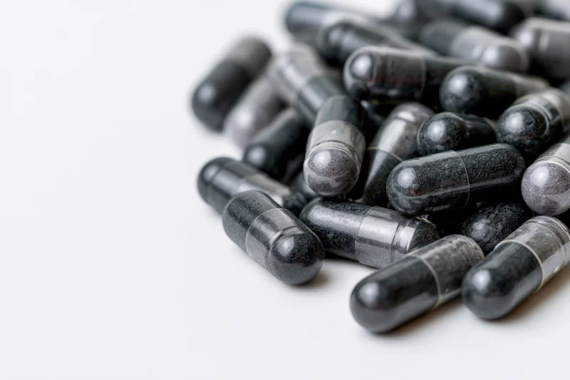 Dark charcoal and grey supplement capsules scattered loosely on white surface