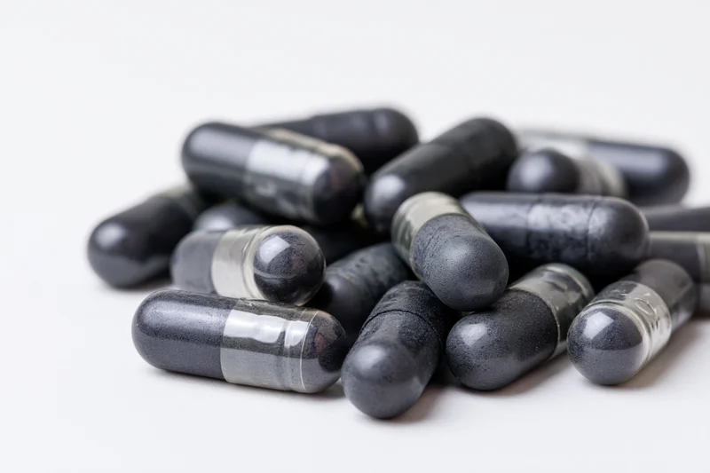 Dark charcoal and grey supplement capsules scattered loosely on white background