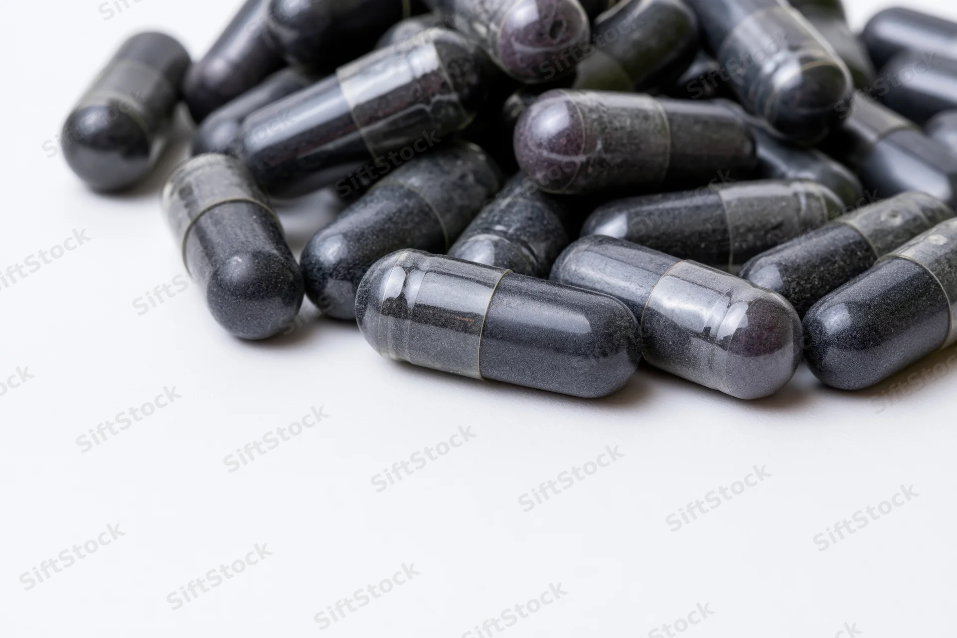 Dark charcoal and grey supplement capsules scattered loosely on white background
