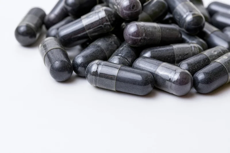 Dark charcoal and grey supplement capsules scattered loosely on white background