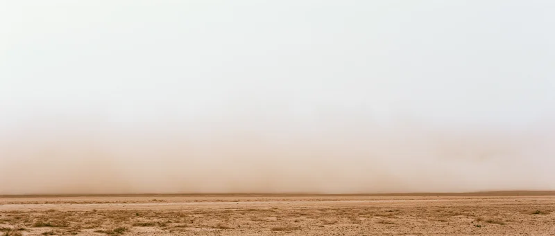 Dense dust cloud billowing low across dry desert floor wide