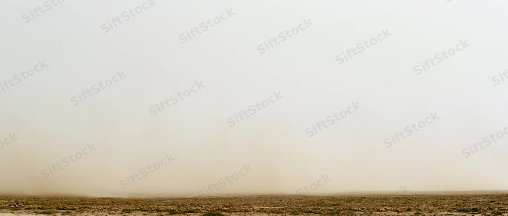 Dense dust cloud billowing low across dry desert floor wide