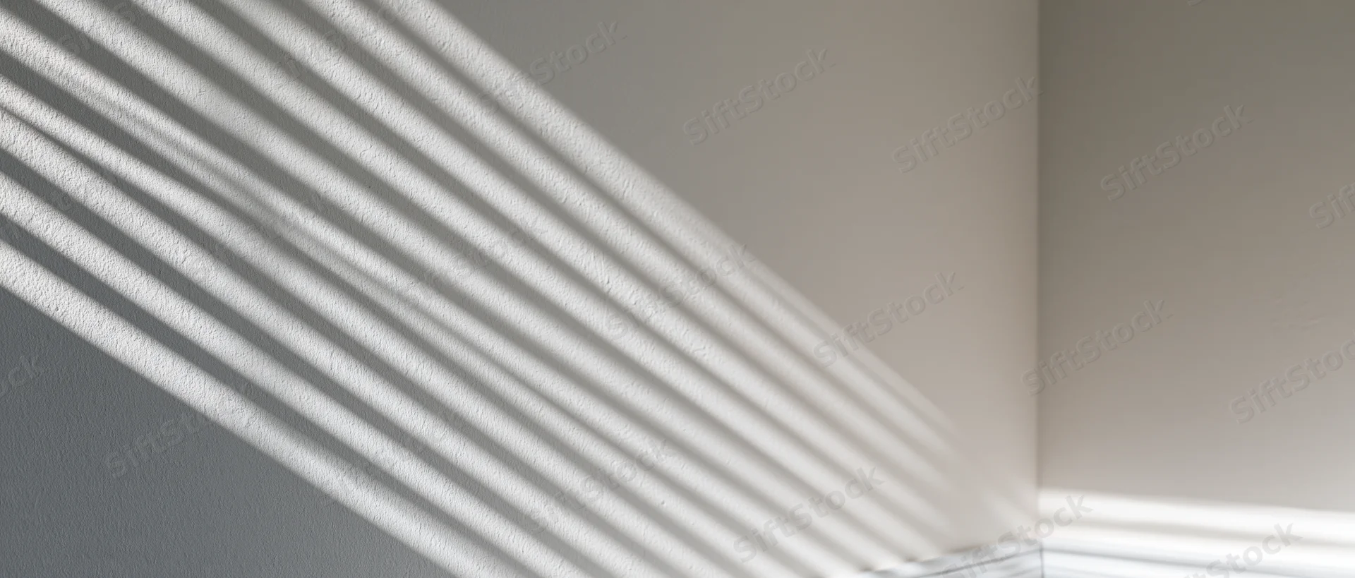 Diagonal light casting parallel shadow stripes across a white interior wall corner