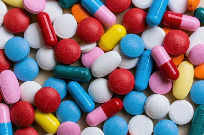 Scattered pharmaceutical pills and capsules in various colors and forms on a flat surface