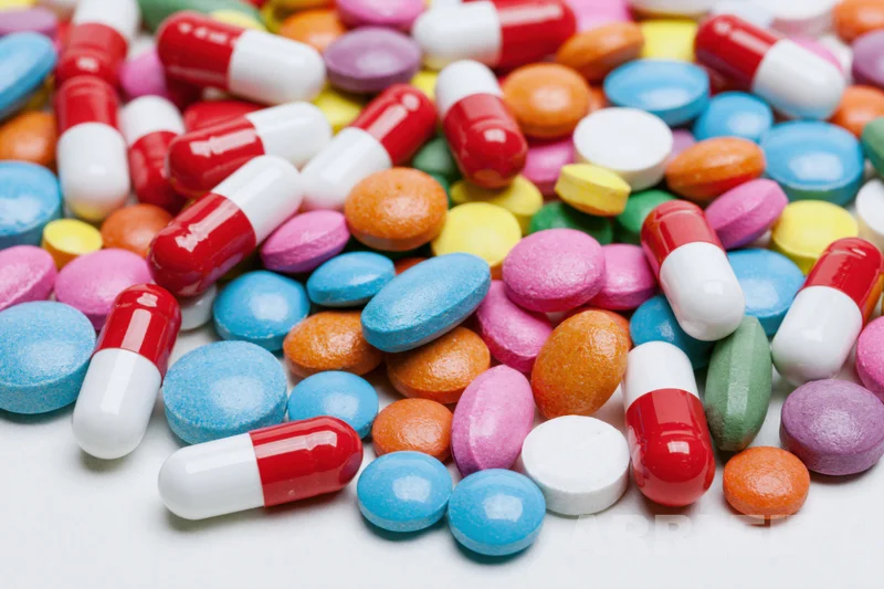 Assorted pharmaceutical pills and capsules scattered on white surface